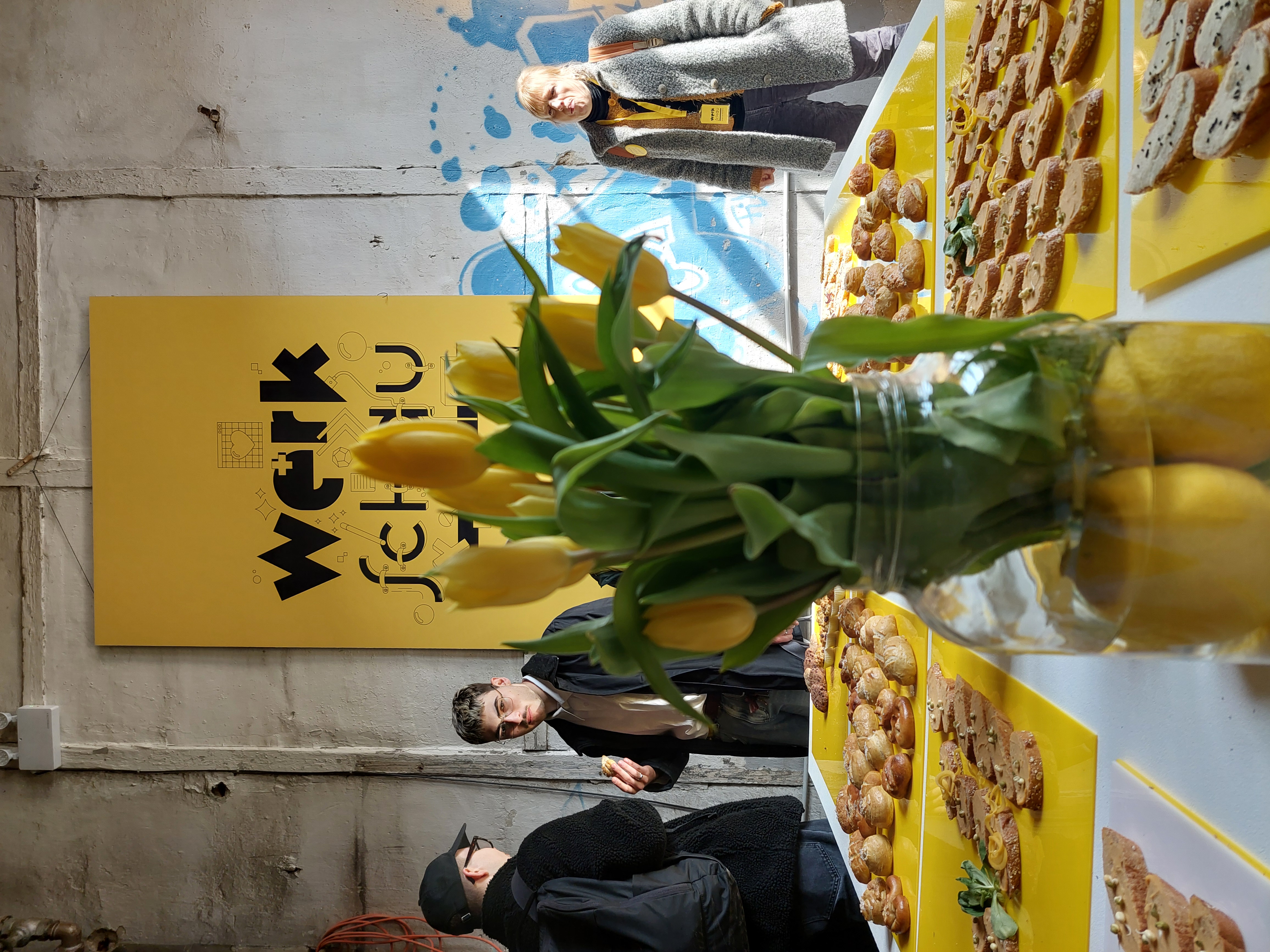 gelbe Tulpen in Vase vor gelbem Plakat Werkschau