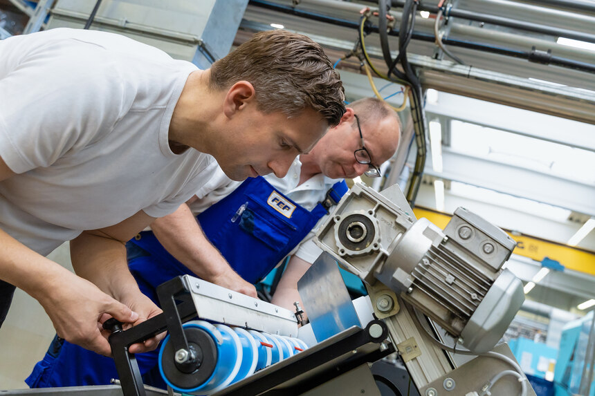 Minister Martin Dulig und ein Mitarbeiter bei FEP arbeiten an einer Maschine mit einer blauen Rolle und weißem Gewinde.