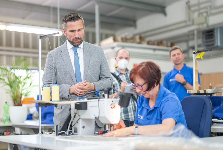 Wirtschaftsminister Martin Dulig spricht mit einer Mitarbeiterin der BATEX Technische Textilien GmbH, die an einer Nähmaschine arbeitet.