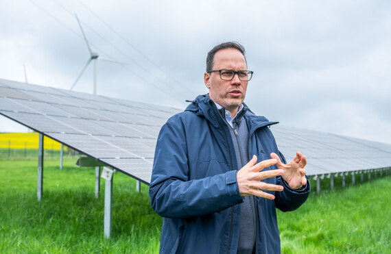 Minister Dirk Panter spricht, im Hintergrund sind eine Photovoltaikfreiflächenanlage und Windräder.