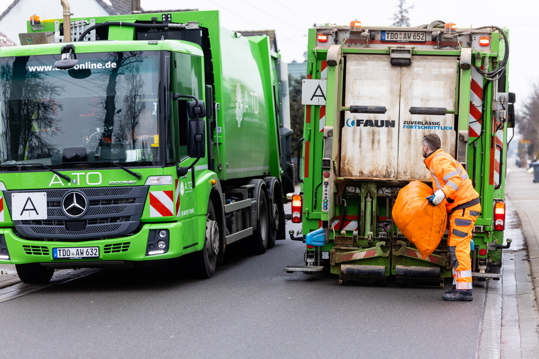 Minister Martin Dulig hebt orangene Abfallsäcke in ein Müllauto.